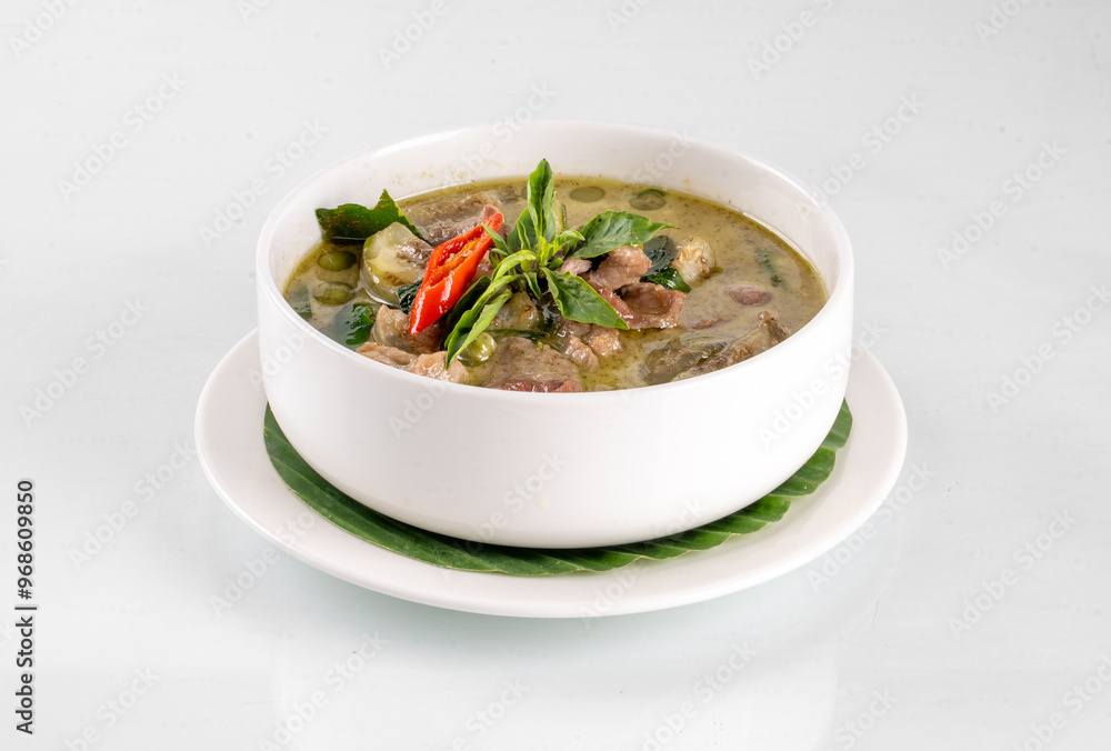 A bowl of delicious Thai green curry with fresh herbs and spices, presented on a white plate with a garnish of red chili peppers and leaves. A bowl of delicious Thai green curry with fresh herbs and spices, presented on a white plate with a garnish of red chili peppers and leaves.