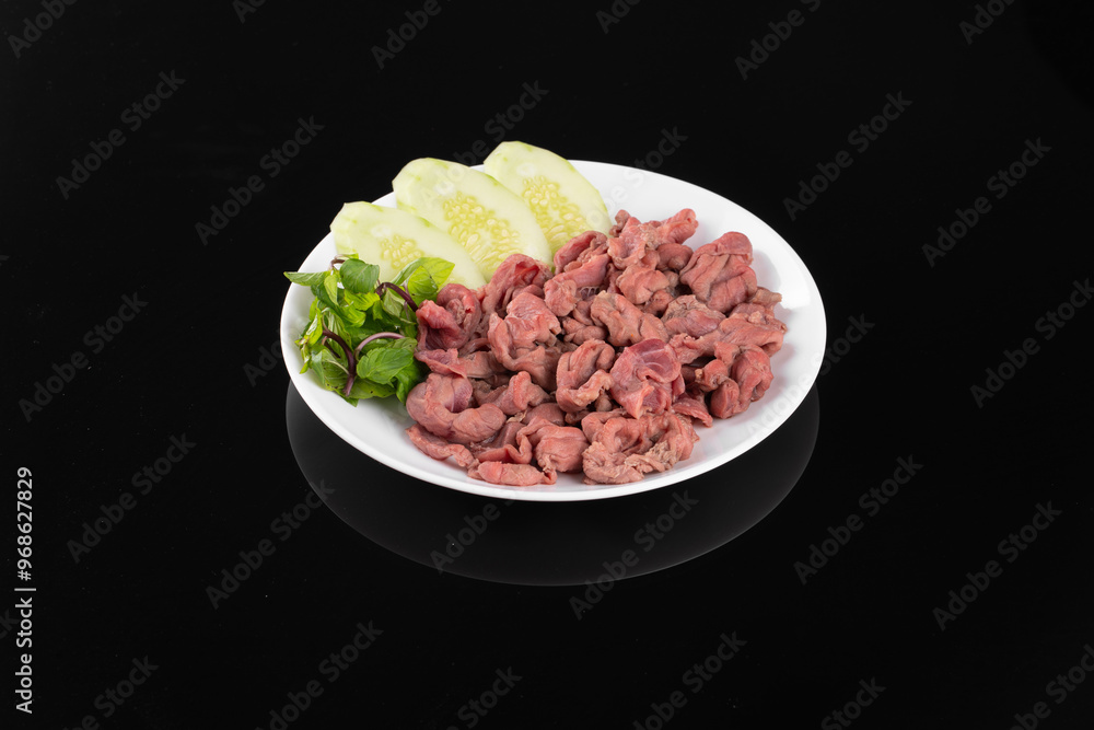 A plate of finely chopped cooked meat paired with sliced cucumbers and fresh herbs, presented on a black background. A plate of finely chopped cooked meat paired with sliced cucumbers and fresh herbs, presented on a black background.