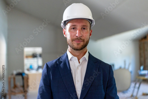 A confident architect wearing a safety helmet stands proudly at a bustling house remodeling site, showcasing his professionalism and unwavering commitment to safety and the overall project success