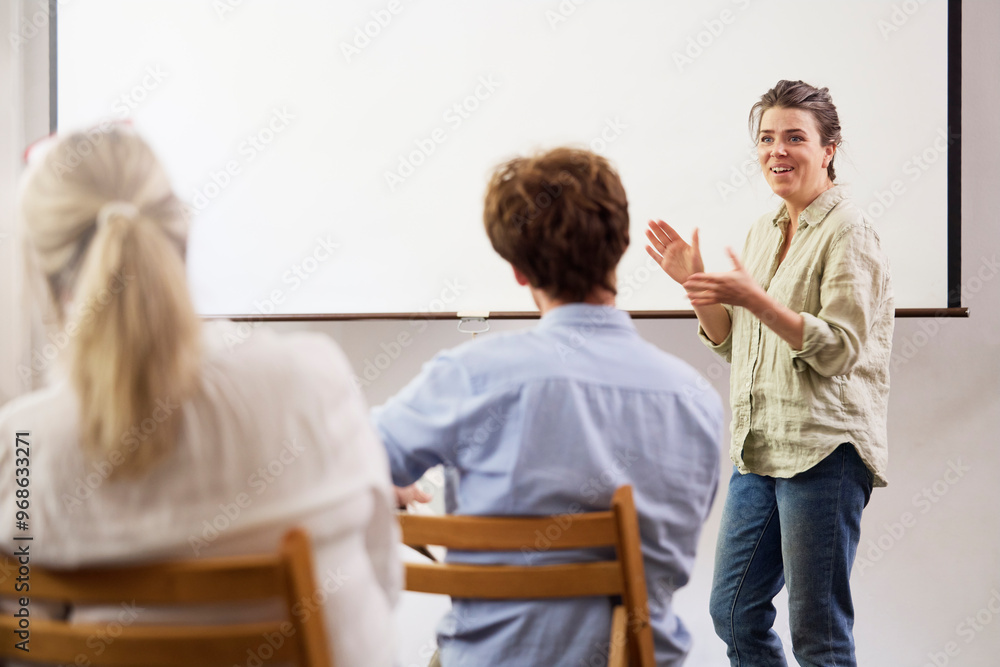 Smiling businesswoman giving presentation to colleagues against blank projection screen at office Smiling businesswoman giving presentation to colleagues against blank projection screen at office