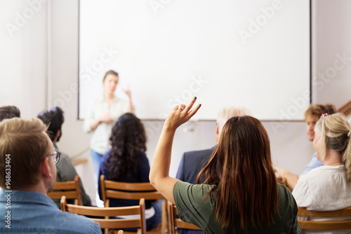 Businesswoman with hand raised sitting behind colleagues during meeting in office
