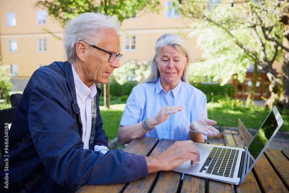 Senior woman explaining while senior man using laptop in park Senior woman explaining while senior man using laptop in park