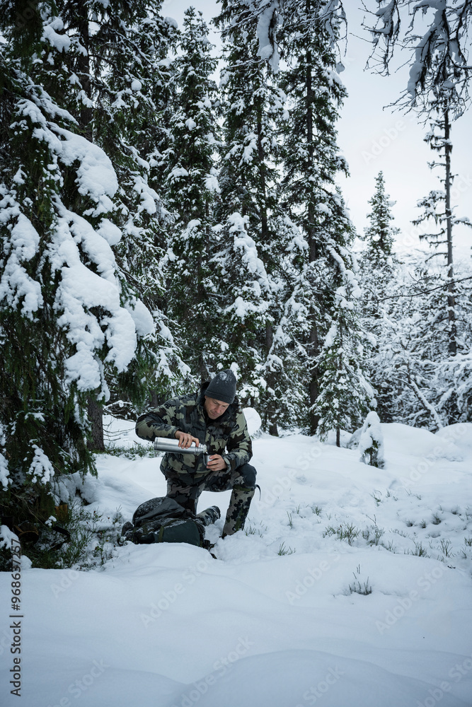 Hunter pouring coffee in cup by trees in forest during winter Hunter pouring coffee in cup by trees in forest during winter