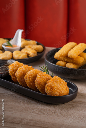 A variety of fried appetizers, including chicken nuggets, mozzarella sticks, and potato croquettes, elegantly arranged on black plates. photo