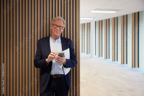 Portrait of smiling senior businessman standing against wall in office lobby photo