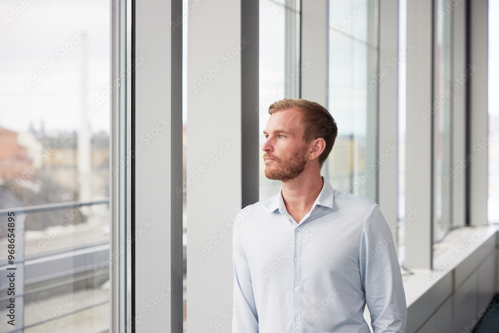 Thoughtful young businessman looking through window Thoughtful young businessman looking through window