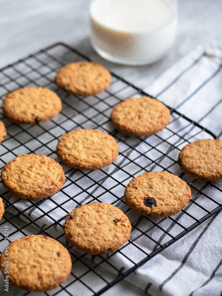 Freshly baked oatmeal cookies cooling on a black wire rack, with a light background and soft natural lighting. The cookies are golden brown with hints of raisins and a crispy texture, creating a cozy Freshly baked oatmeal cookies cooling on a black wire rack, with a light background and soft natural lighting. The cookies are golden brown with hints of raisins and a crispy texture, creating a cozy