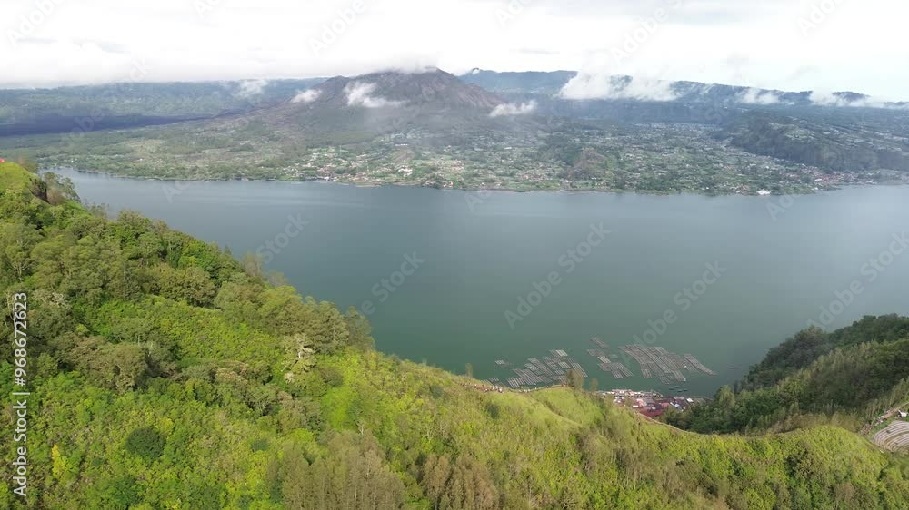 Lush green hills and a calm lake with misty mountains in the distance, aerial view Lush green hills and a calm lake with misty mountains in the distance, aerial view