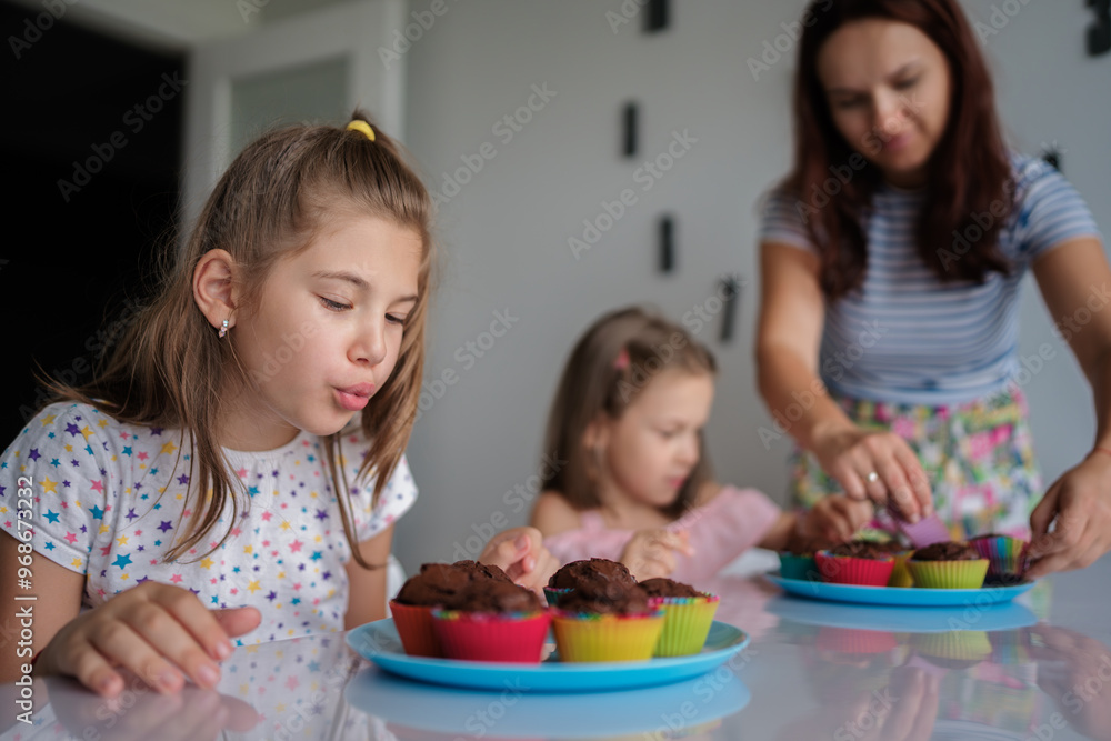 A joyful scene of a mother and two daughters baking chocolate cupcakes. The children are excited as they decorate the treats, enjoying quality family time in a cozy kitchen setting. A joyful scene of a mother and two daughters baking chocolate cupcakes. The children are excited as they decorate the treats, enjoying quality family time in a cozy kitchen setting.