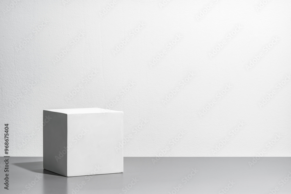 A simple white cube on a gray surface against a blank wall A simple white cube on a gray surface against a blank wall