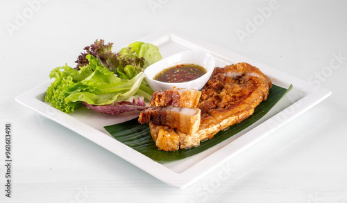 Crispy pork belly served with fresh salad greens and dipping sauce on a white plate. Perfect for food and restaurant themes.