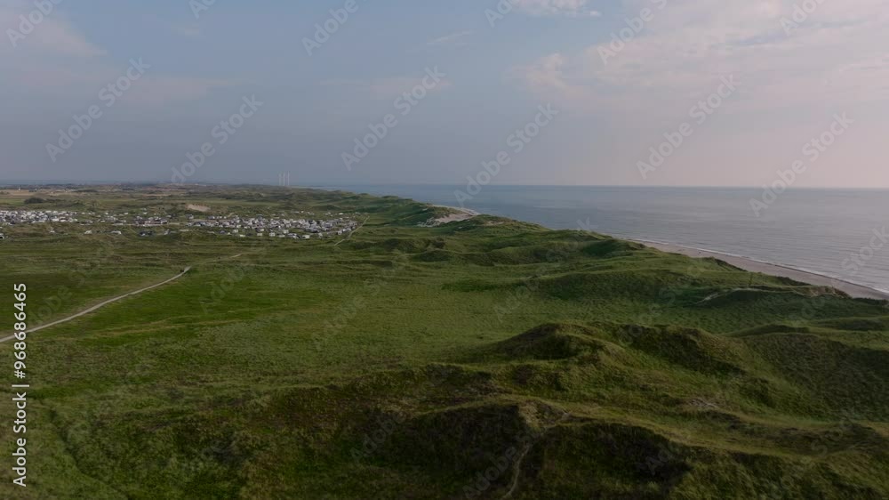 Aerial views reveal Denmark's breathtaking coastline, where lush dunes blend with sandy shores along the North Sea. A quaint town enhances the idyllic scenery in the distance Aerial views reveal Denmark's breathtaking coastline, where lush dunes blend with sandy shores along the North Sea. A quaint town enhances the idyllic scenery in the distance