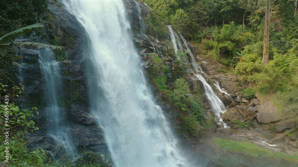 Obraz premium Majestic waterfall cascading over rugged cliffs into lush forest below, showcasing beauty of untouched nature. Nature and Wilderness.