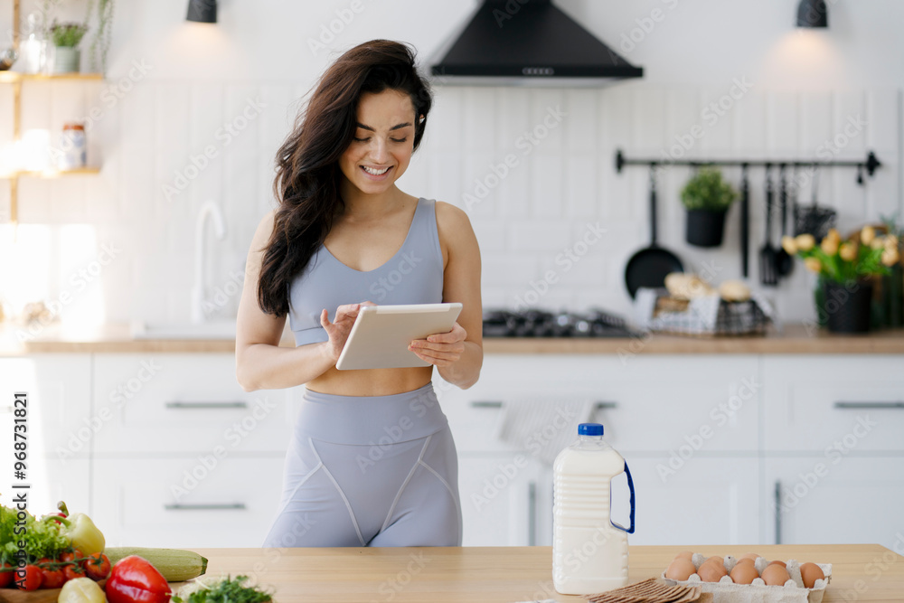 Young woman checking online recipe on tablet while preparing healthy meal in kitchen Young woman checking online recipe on tablet while preparing healthy meal in kitchen