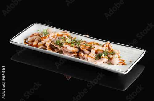 Deliciously plated gourmet dish of sliced grilled meat with garnish on a rectangular white plate, against a black background.