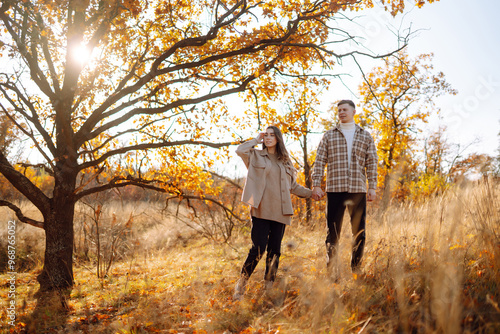 A couple enjoys a joyful moment together on a serene autumn day in a colorful forest setting with vibrant foliage and soft sunlight. The concept of youth, love and lifestyle.