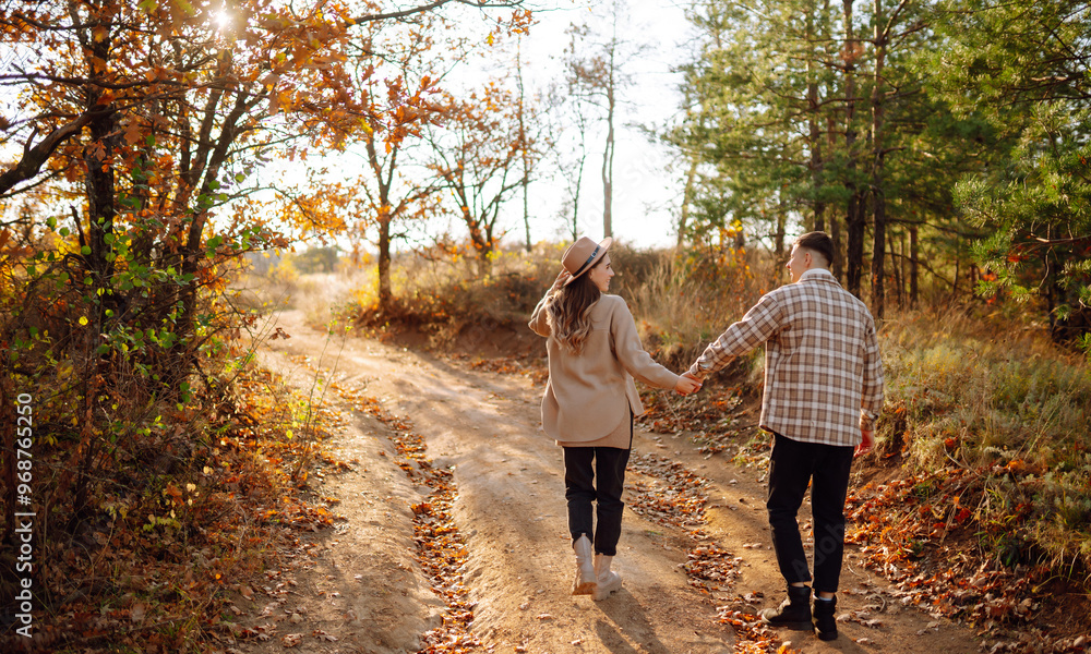 Fototapeta premium A couple enjoys a joyful moment together on a serene autumn day in a colorful forest setting with vibrant foliage and soft sunlight. The concept of youth, love and lifestyle.