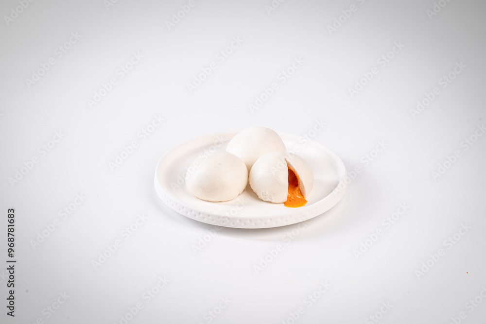 Steamed buns filled with custard, placed on a white plate against a plain background, showcasing traditional Asian cuisine. Steamed buns filled with custard, placed on a white plate against a plain background, showcasing traditional Asian cuisine.
