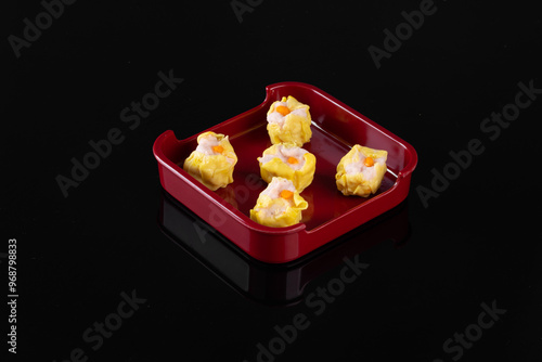 Five delicious dim sum dumplings served in a red square dish on a black background, showcasing traditional Asian cuisine. photo