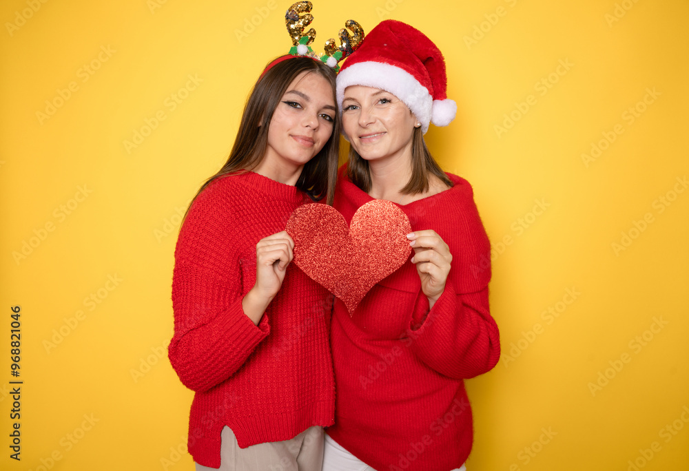 Happy family in Christmas caps. Mother and daughter making heart figure with hands. Happy family in Christmas caps. Mother and daughter making heart figure with hands.