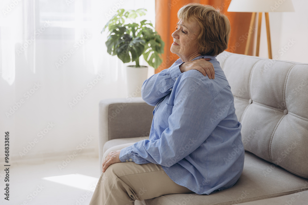 Senior woman sitting on sofa with shoulder pain. Elderly woman is enduring awful ache. Old woman suffering from shoulder injury, health problem concept Senior woman sitting on sofa with shoulder pain. Elderly woman is enduring awful ache. Old woman suffering from shoulder injury, health problem concept