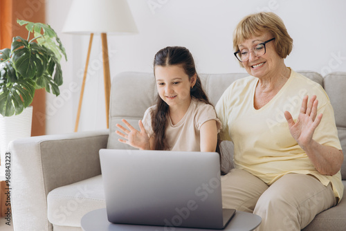 Granddaughter with grandmother waving hand during video call. Old woman sitting with her little granddaughter making a video call.