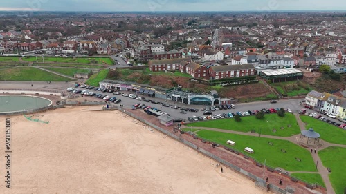 An aerial view captures a coastal town with a mix of residential and commercial buildings. The beachfront parking is filled with cars. photo