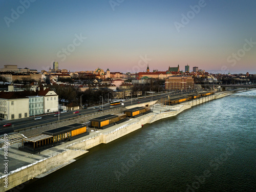 Panoramic view of Warsaw at dawn, featuring the Vistula River and modern boulevards. The historic Old Town and Royal Castle are illuminated by soft morning light, blending the city’s modern and histor photo