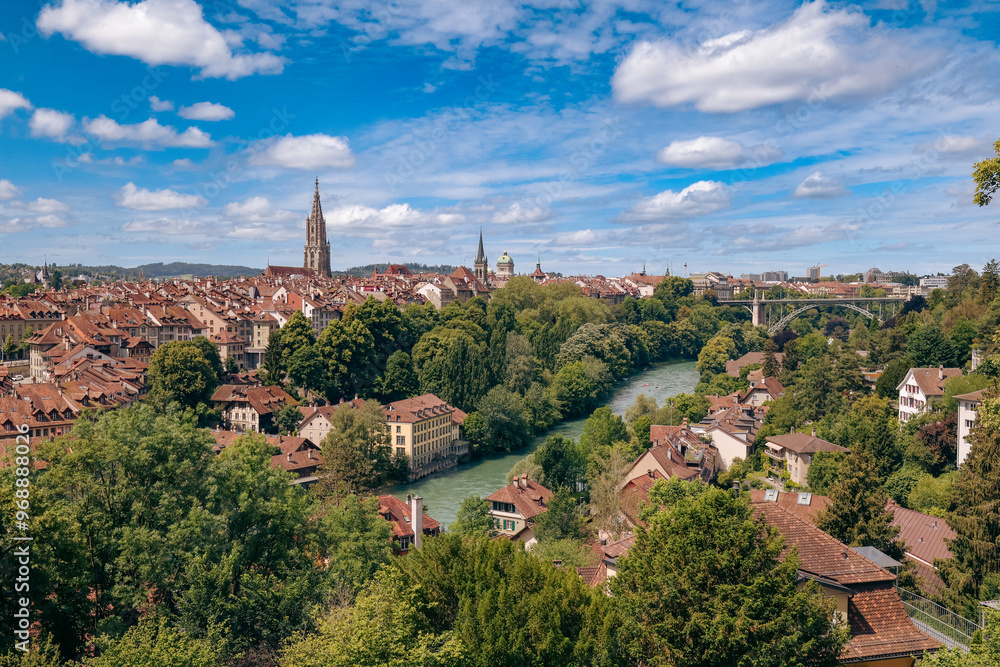 A panoramic view of Bern, Switzerland showcasing the Aare River, medieval architecture, and lush greenery under a bright blue sky A panoramic view of Bern, Switzerland showcasing the Aare River, medieval architecture, and lush greenery under a bright blue sky