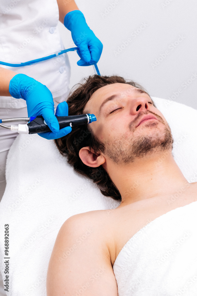 Man receiving a hydrafacial treatment in a modern cosmetic center. Innovative skin hydration and cleansing for visible rejuvenation. Perfect for promoting advanced skincare solutions. Man receiving a hydrafacial treatment in a modern cosmetic center. Innovative skin hydration and cleansing for visible rejuvenation. Perfect for promoting advanced skincare solutions.