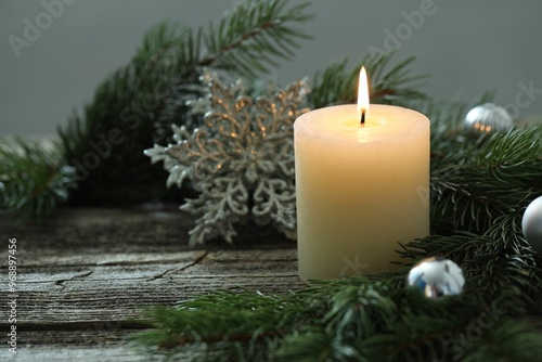 Burning candle, baubles and fir tree branches on wooden table, closeup. Space for text