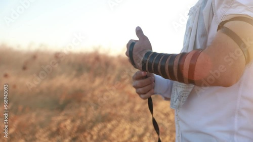 Arm Tefillin - jewish phylacteries. close up shot on Jewish man with prayer shawl Talit wrapping his hand with leather string using Tfillin. Spirtual ritual. (Teffilin, Tefilin, Tfilin) photo