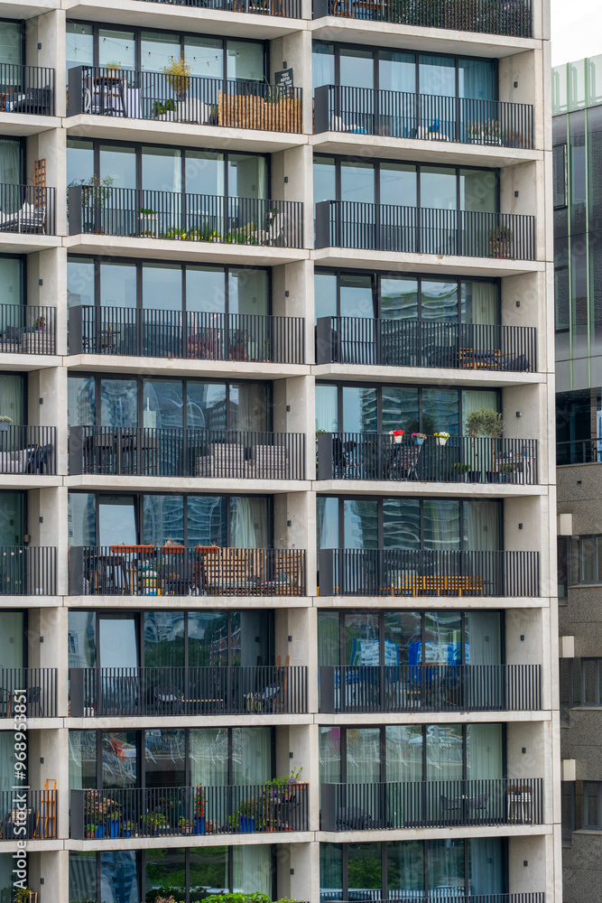 Rows of balconies and large windows of a tall contemporary apartment building, each adorned with different items, represent urban living, diversity, and modern lifestyle in Rotterdam