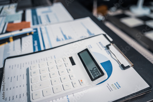 An empty office desk at night with a laptop displaying a business chart, balance sheet, loan calculator, graphs, and monthly budget stats. Blue and black tones, leather office chair.