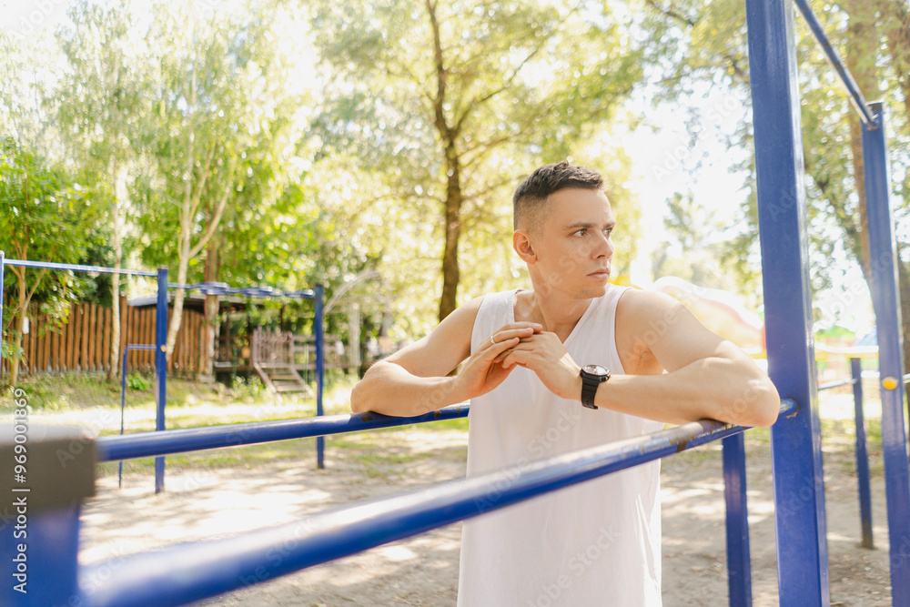 Obraz premium Handsome pumped up young male bodybuilder doing exercises on horizontal bar and parallel bars outdoors on the street. Beautiful male body shapes, beauty and health, training and motivation