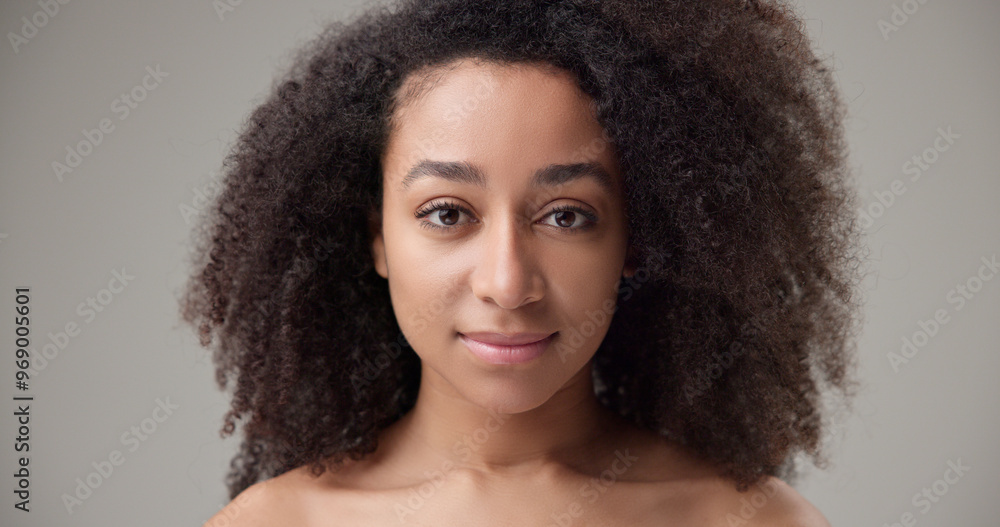 Beauty and healthcare - beautiful African American woman with curly afro hairstyle and clean, healthy skin, standing on a gray studio background opening and closing her eyes looking at the camera Beauty and healthcare - beautiful African American woman with curly afro hairstyle and clean, healthy skin, standing on a gray studio background opening and closing her eyes looking at the camera