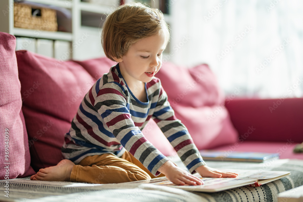 Cute little boy reading books on the sofa at home on a bright sunny afternoon. Daytime care creative activity. Kids having fun. Cute little boy reading books on the sofa at home on a bright sunny afternoon. Daytime care creative activity. Kids having fun.