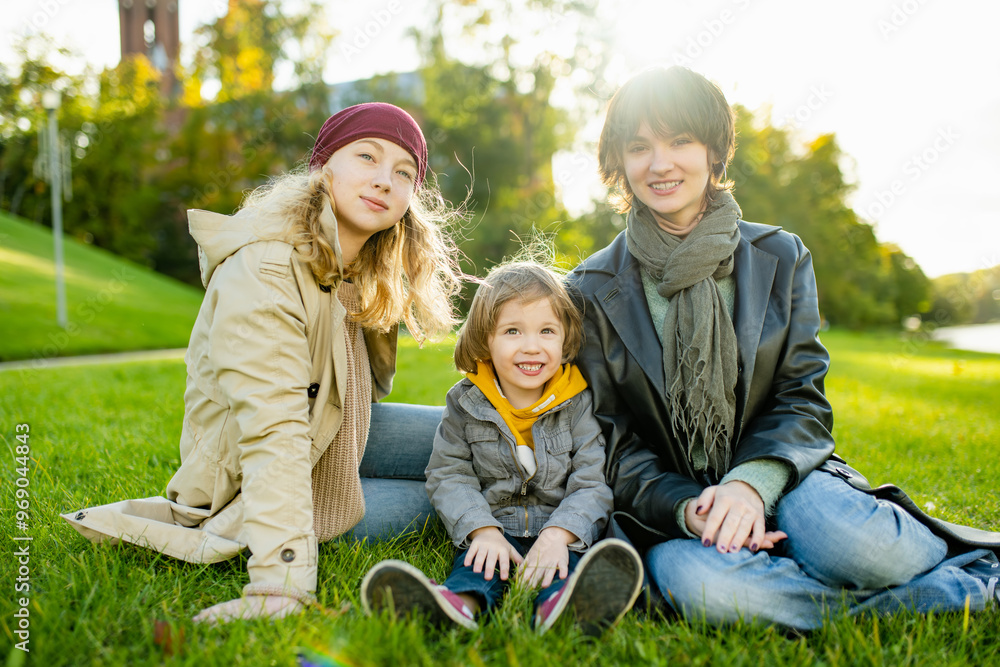 Fototapeta premium Two big sisters and their toddler brother having fun outdoors. Two young girls with a toddler boy on autumn day.