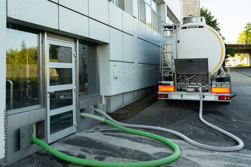 Tank truck delivers liquid to facility through hoses on sunny day photo