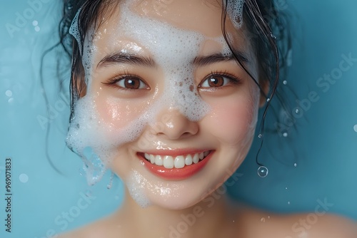 Smiling woman washing face with foam, fresh skincare routine, glowing and clean beauty on blue background 