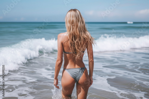 A woman in a bikini stands on the beach, looking out at the ocean. Scene is relaxed and carefree, as the woman is enjoying her time at the beach