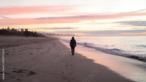Lone traveler walking along an empty beach at sunrise