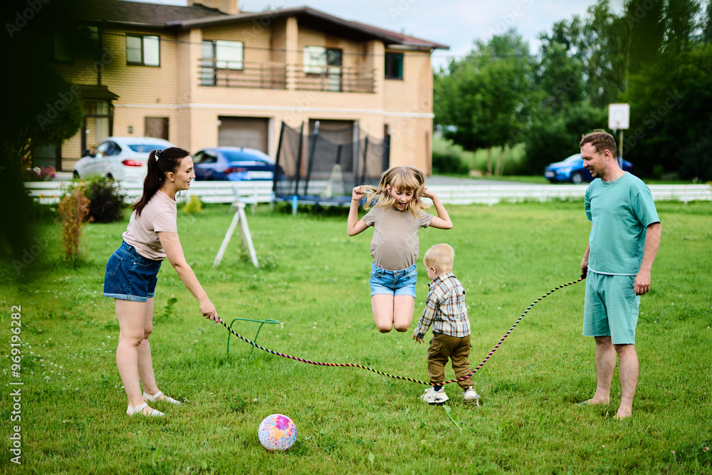 Obraz premium Happy family spending weekend in their backyard jumping rope and playing ball