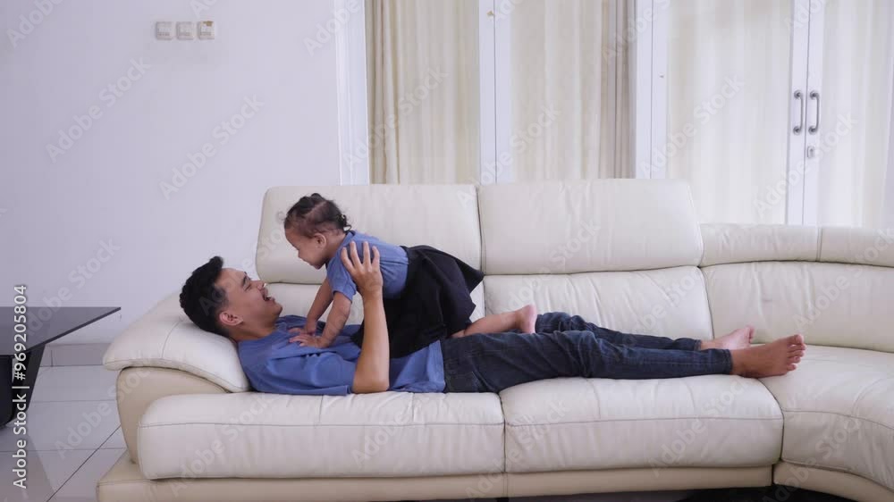 Happy young father and his little daughter playing lying on the sofa, having fun and spending time together.