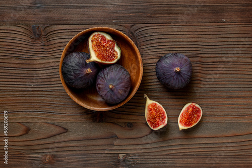 Fresh ripe figs in a wooden bowl on dark wooden table, top view