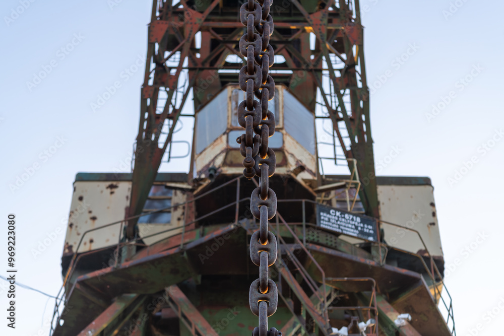 Closeup of a rusty chain on an old industrial harbor crane, highlighting the wear and age of the metal components Closeup of a rusty chain on an old industrial harbor crane, highlighting the wear and age of the metal components