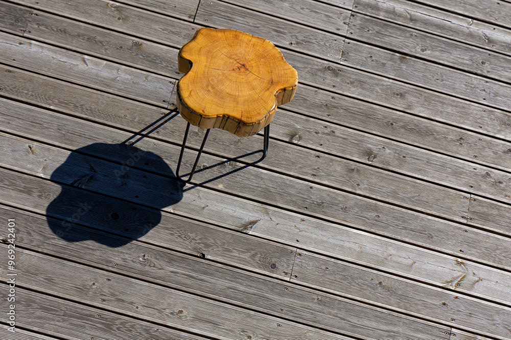 A coffe table made of a light wood trunk against the background of wooden terrace boards. The tree rings of the trunk are clearly visible. A shot of the table from above, taken on a sunny day.