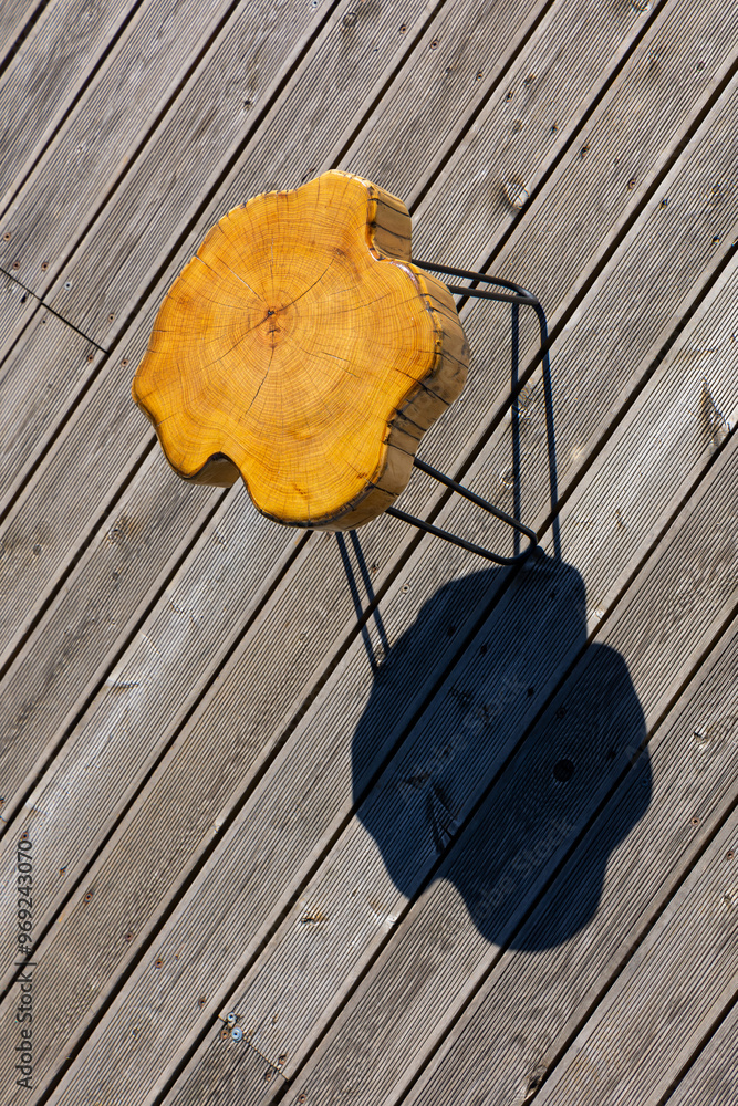 A coffe table made of a light wood trunk against the background of wooden terrace boards. The tree rings of the trunk are clearly visible. A shot of the table from above, taken on a sunny day.