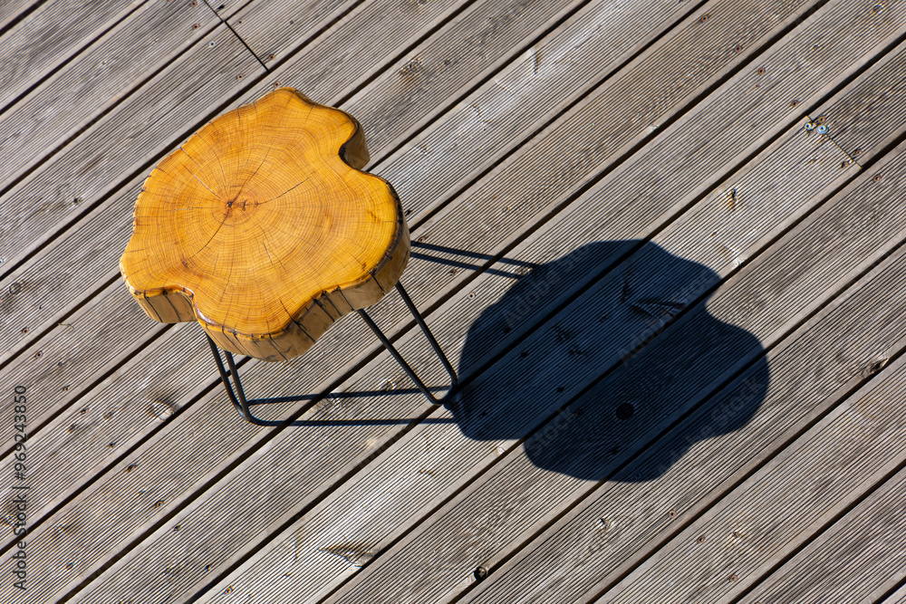 A coffe table made of a light wood trunk against the background of wooden terrace boards. The tree rings of the trunk are clearly visible. A shot of the table from above, taken on a sunny day.