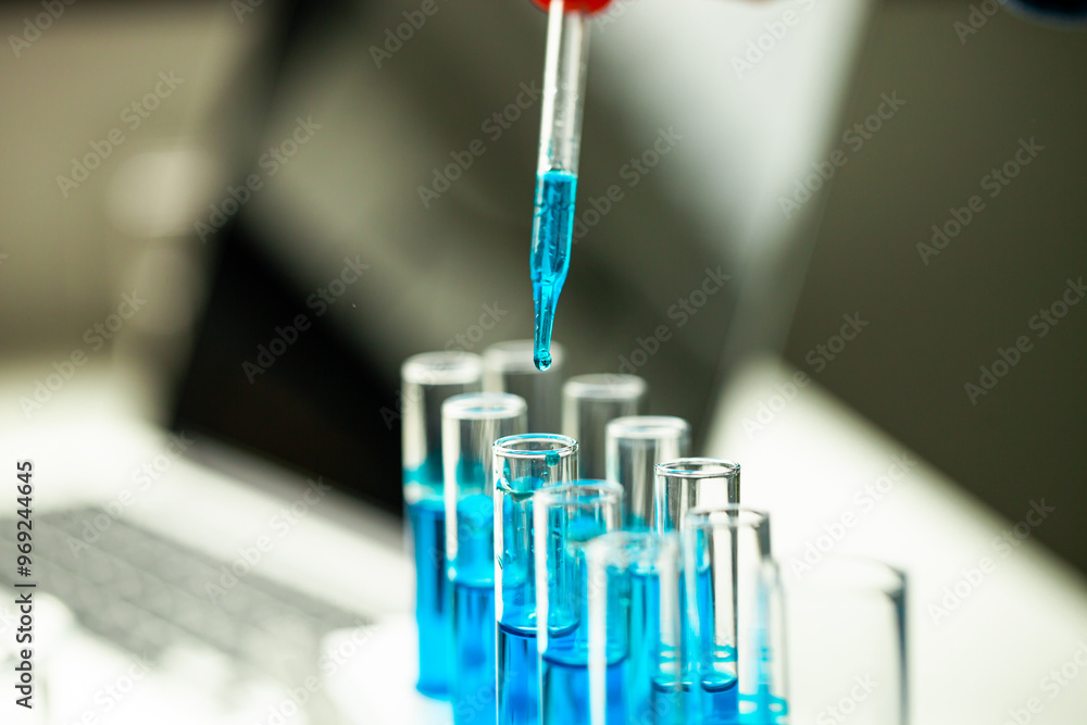 A person is pouring blue liquid into a series of test tubes. Concept of scientific experimentation and precision A person is pouring blue liquid into a series of test tubes. Concept of scientific experimentation and precision